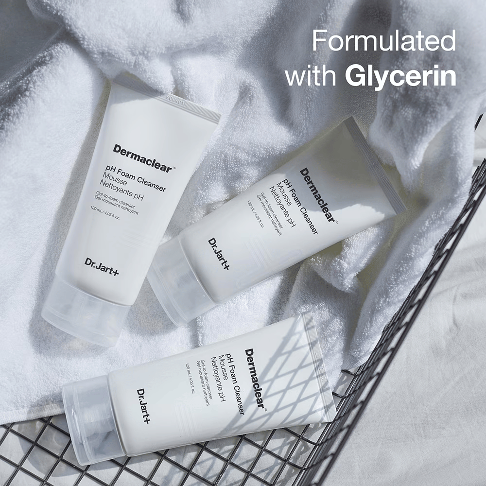 Três tubos de Dr.Jart+ Dermaclear pH Foam Cleanser estão sobre uma toalha de felpo branca em uma cesta de metal, com o texto "Formulated with Glycerin" no canto superior.