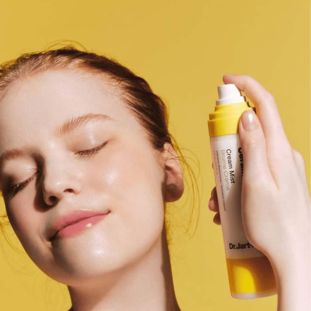 Uma mulher segura uma garrafa de Dr. Jart+ Ceramidin Cream Mist 110ml no rosto, promovendo seus benefícios de aumento de umidade e formulação vegana.