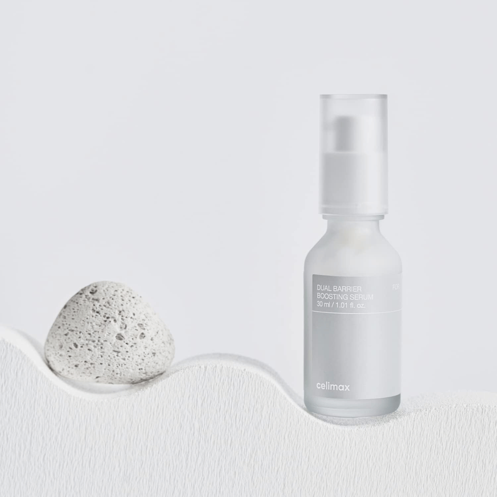 Celimax Dual Barrier Boosting Serum colocado em tecido com pedra, imagem de produto tranquila que sinaliza hidratação e fortalecimento da barreira da pele.