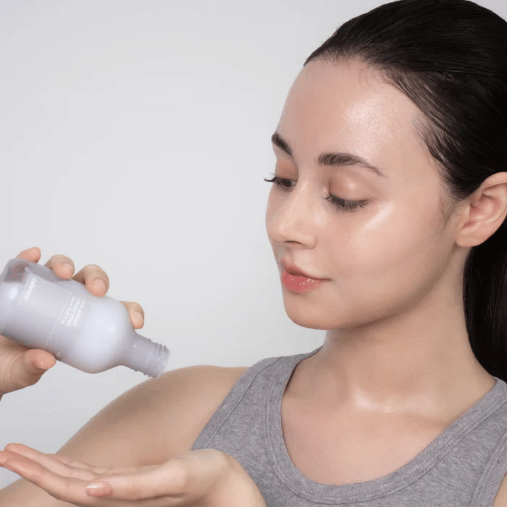 Mulher com pele brilhante e hidratada aplica Celimax Dual Barrier Creamy Toner ao verter o produto na palma da mão antes da sua rotina de cuidados de pele.