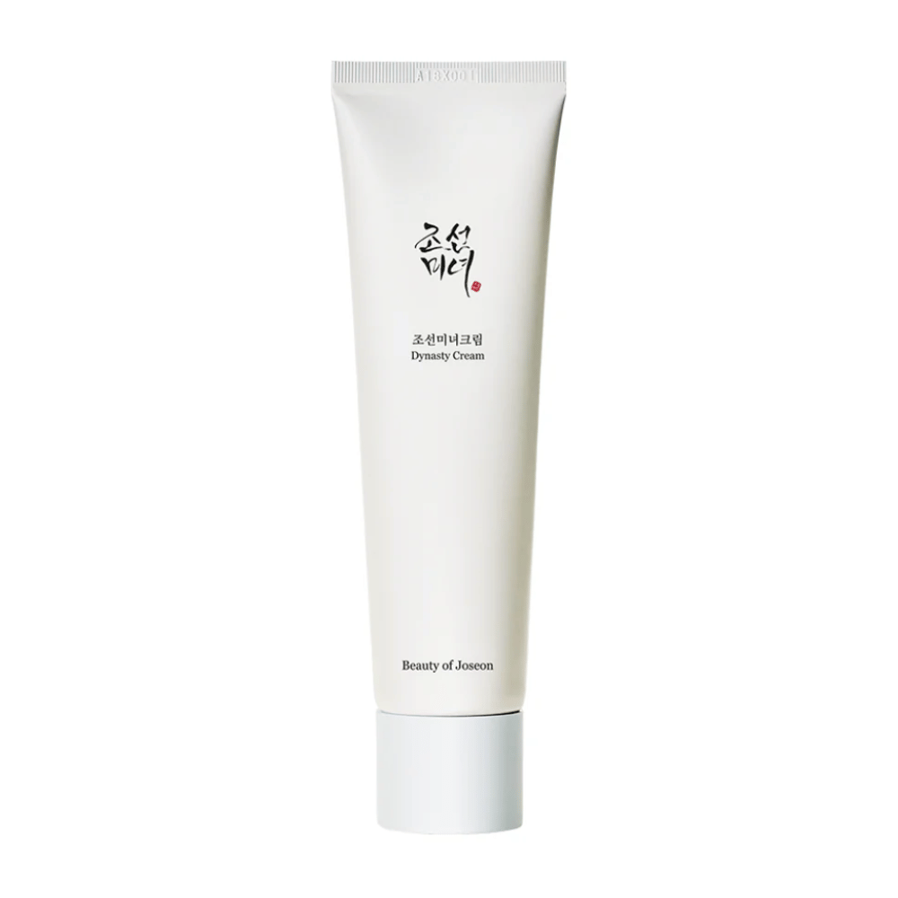 A imagem mostra um tubo de "Beauty of Joseon Dynasty Cream". O tubo branco e esguio tem elementos de design minimalistas, incluindo texto elegante em preto e vermelho. Este produto de cuidados com a pele promete nutrir e vitalizar a pele, refletindo os segredos de beleza históricos da dinastia Joseon.