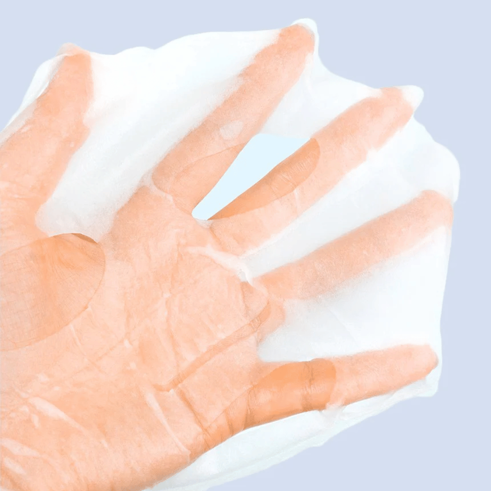 Uma máscara facial transparente e úmida é segurada em uma mão contra um fundo azul claro. A máscara é projetada para cobrir o rosto com espaços para os olhos e a boca.