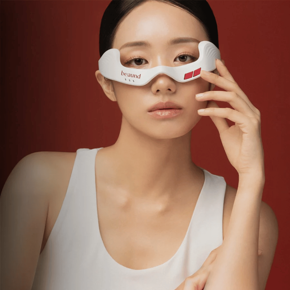 Imagem com modelo em que uma pessoa usa Beaund Eye Rejuv, um dispositivo LED futurista para a área à volta dos olhos, sobre um elegante fundo vermelho.
