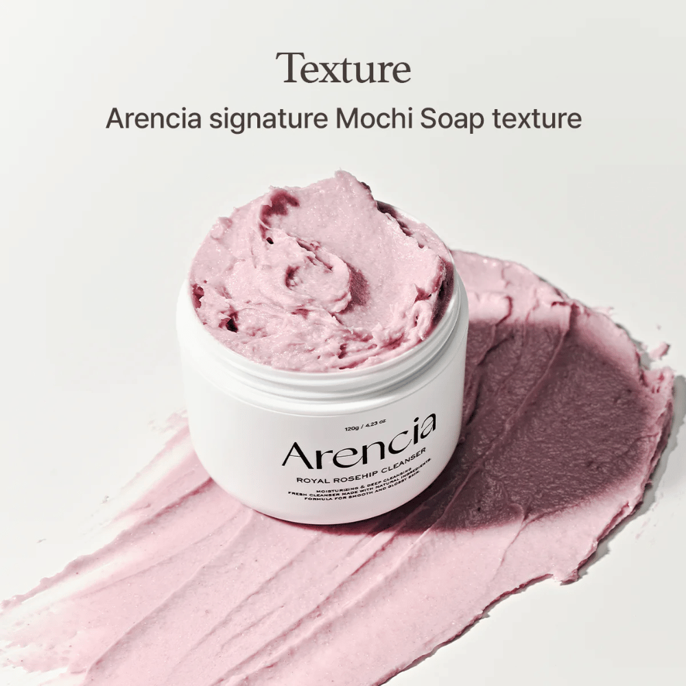 Frasco com Arencia Royal Rosehip Cleanser é visível sobre uma limpeza rosa espalhada com textura semelhante a mochi. O texto acima descreve o produto como a textura assinatura da Arencia.