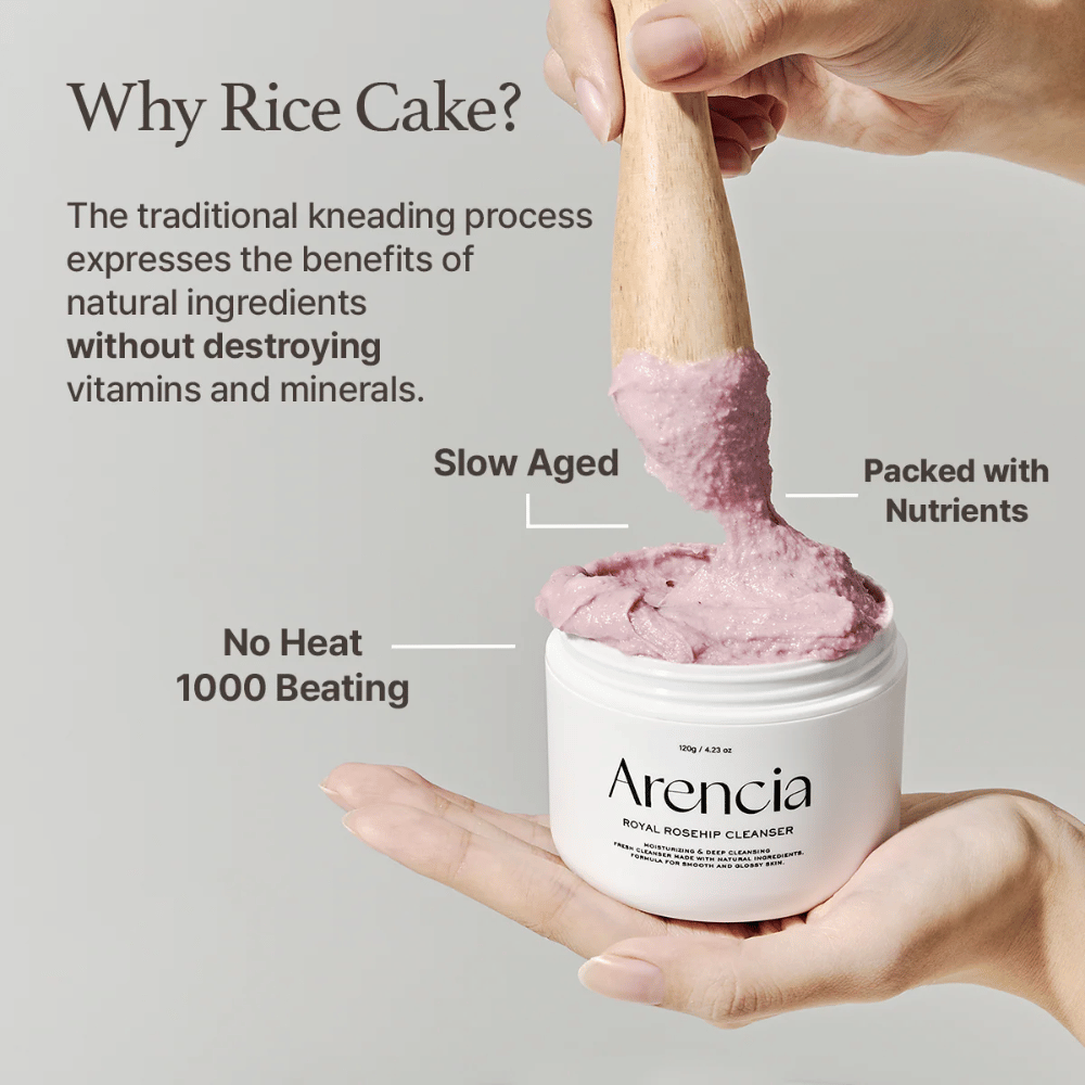 Uma mão segura um frasco aberto de Arencia Royal Rosehip Cleanser, com uma fórmula de limpeza rosa, semelhante a mochi, sendo levantada com uma espátula de madeira – mostrando a textura do produto e o método de fabricação tradicional.