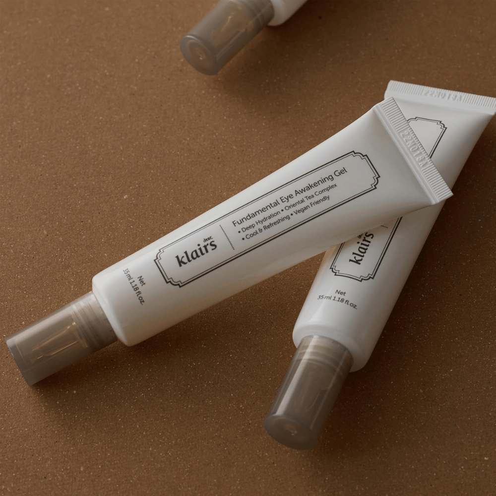 Imagem lifestyle com duas bisnagas de Klairs Fundamental Eye Awakening Gel colocadas sobre um fundo castanho quente. A composição realça o design elegante do produto e a sensação premium, mantendo ao mesmo tempo o foco no cuidado dos olhos e na hidratação.