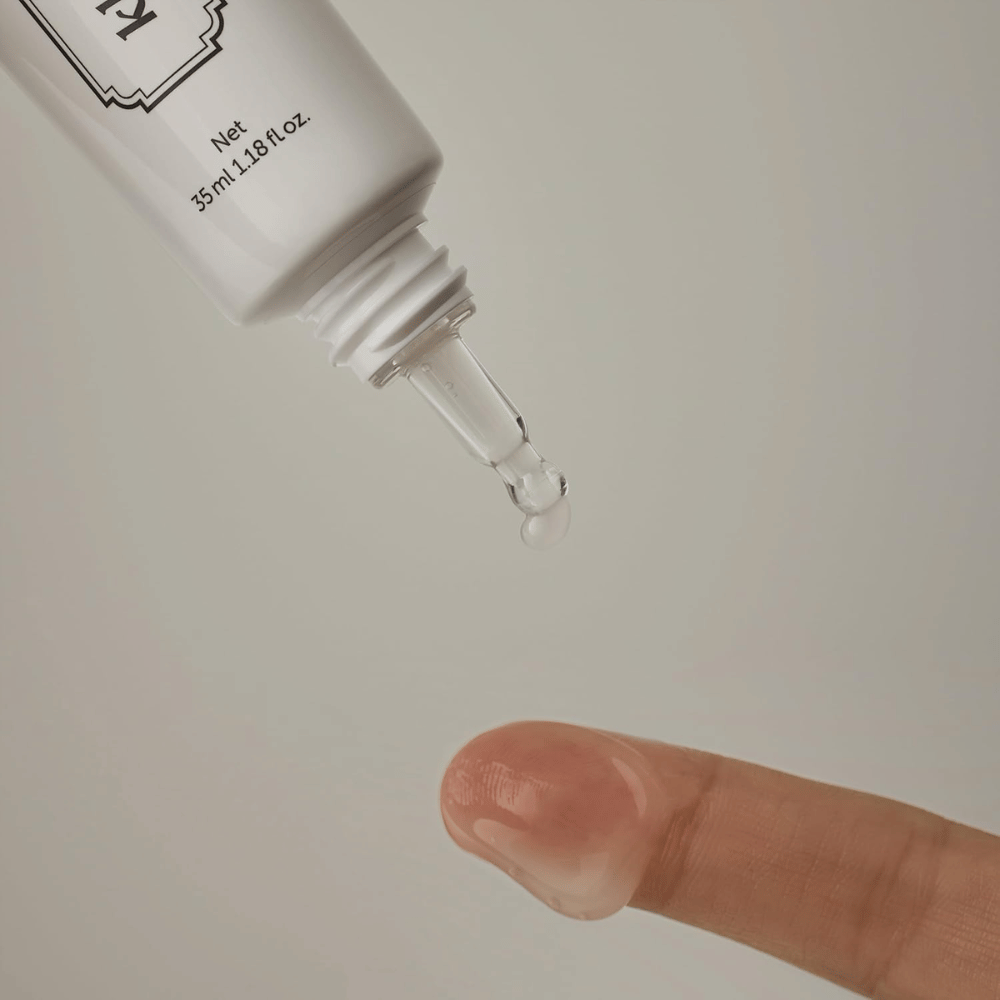 Imagem de detalhe em que um gel claro e leve é aplicado a partir da ponta estreita sobre um dedo. A imagem ilustra a consistência transparente à base de gel do produto e a aplicação precisa na zona do contorno dos olhos.