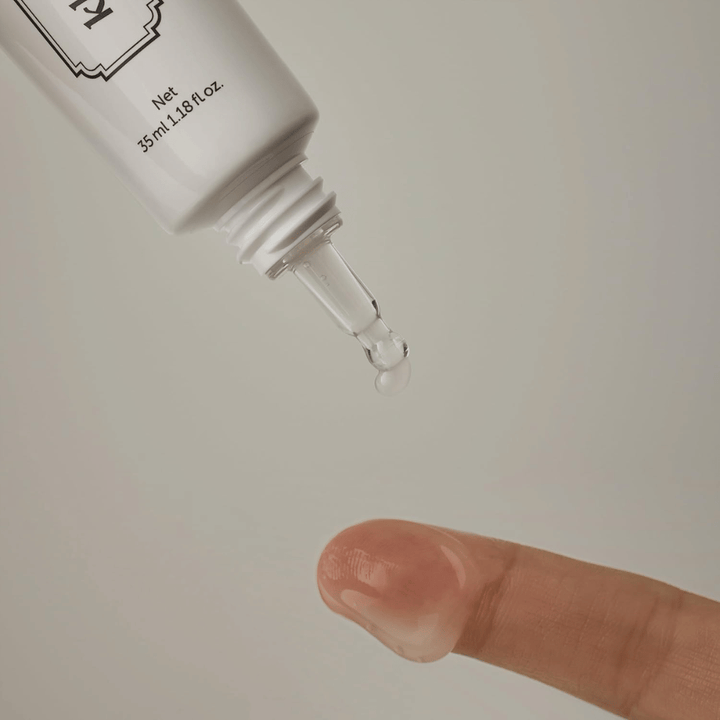 Imagem de detalhe em que um gel claro e leve é aplicado a partir da ponta estreita sobre um dedo. A imagem ilustra a consistência transparente à base de gel do produto e a aplicação precisa na zona do contorno dos olhos.