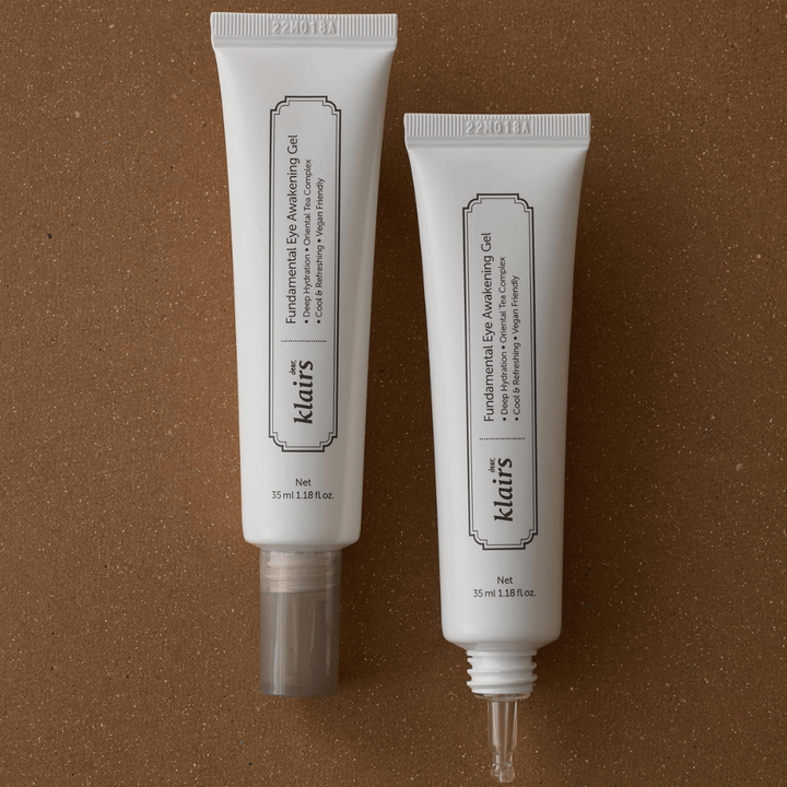 Imagem de produto que mostra Klairs Fundamental Eye Awakening Gel em duas versões – uma bisnaga fechada e uma bisnaga aberta que destaca a ponta aplicadora estreita. A embalagem tem um design branco minimalista e realça o foco do produto na hidratação, na sensação refrescante e no cuidado revitalizante da zona do contorno dos olhos.