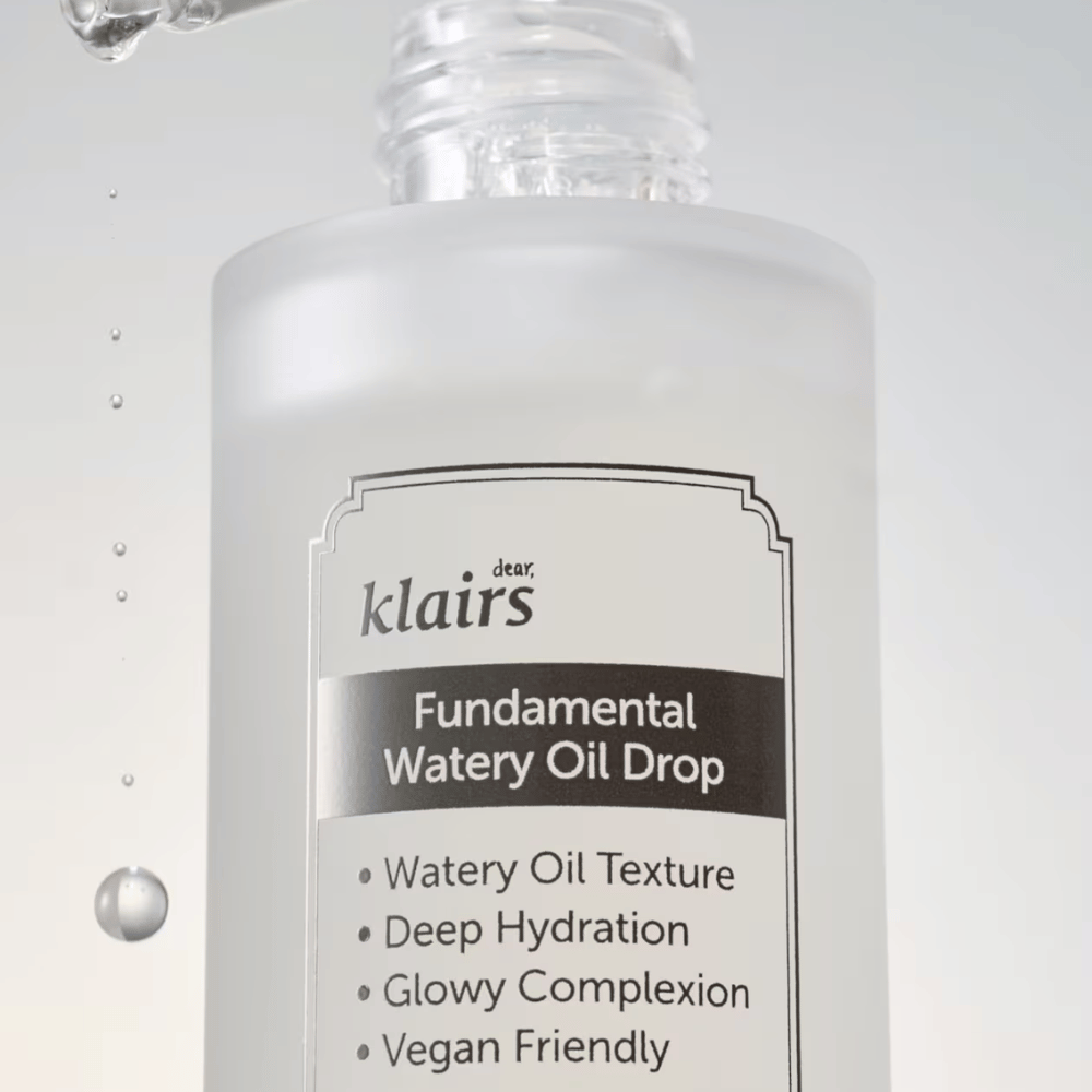 Close-up do frasco Klairs Fundamental Watery Oil Drop, com texto destacando as propriedades do produto como "Textura de Óleo Aquoso", "Hidratação Profunda", "Tez Iluminada" e "Amigável ao Veganismo".