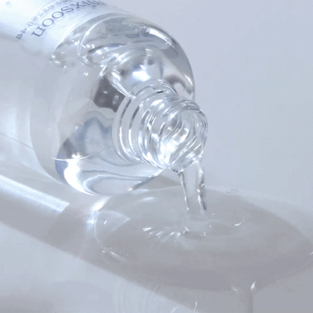 Close-up de soro transparente sendo derramado de uma garrafa Mixsoon Glacier Water Hyaluronic Acid Serum sobre uma superfície brilhante.