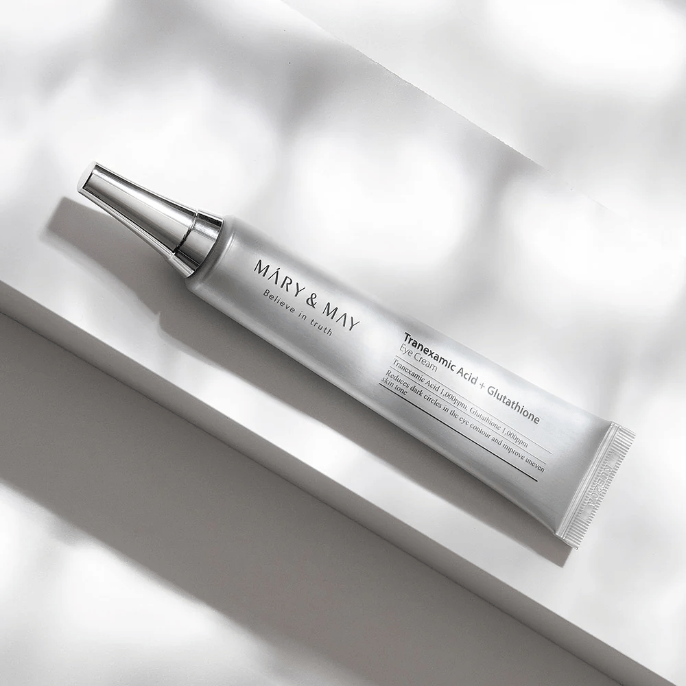Close-up de Mary&May Tranexamic Acid + Glutathione Eye Cream com aplicador de metal, desenvolvido para iluminar olheiras e uniformizar o tom da pele ao redor dos olhos.