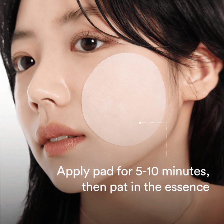 Mulher aplica uma toner pad redonda na bochecha para cuidados de pele hidratantes e iluminadores.