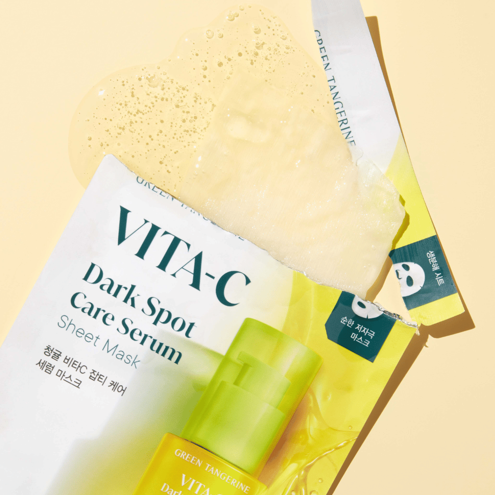 Embalagem aberta do VITA-C Dark Spot Care Serum Sheet mask com uma máscara facial em cima e um frasco de soro verde, todos contra um fundo amarelo.