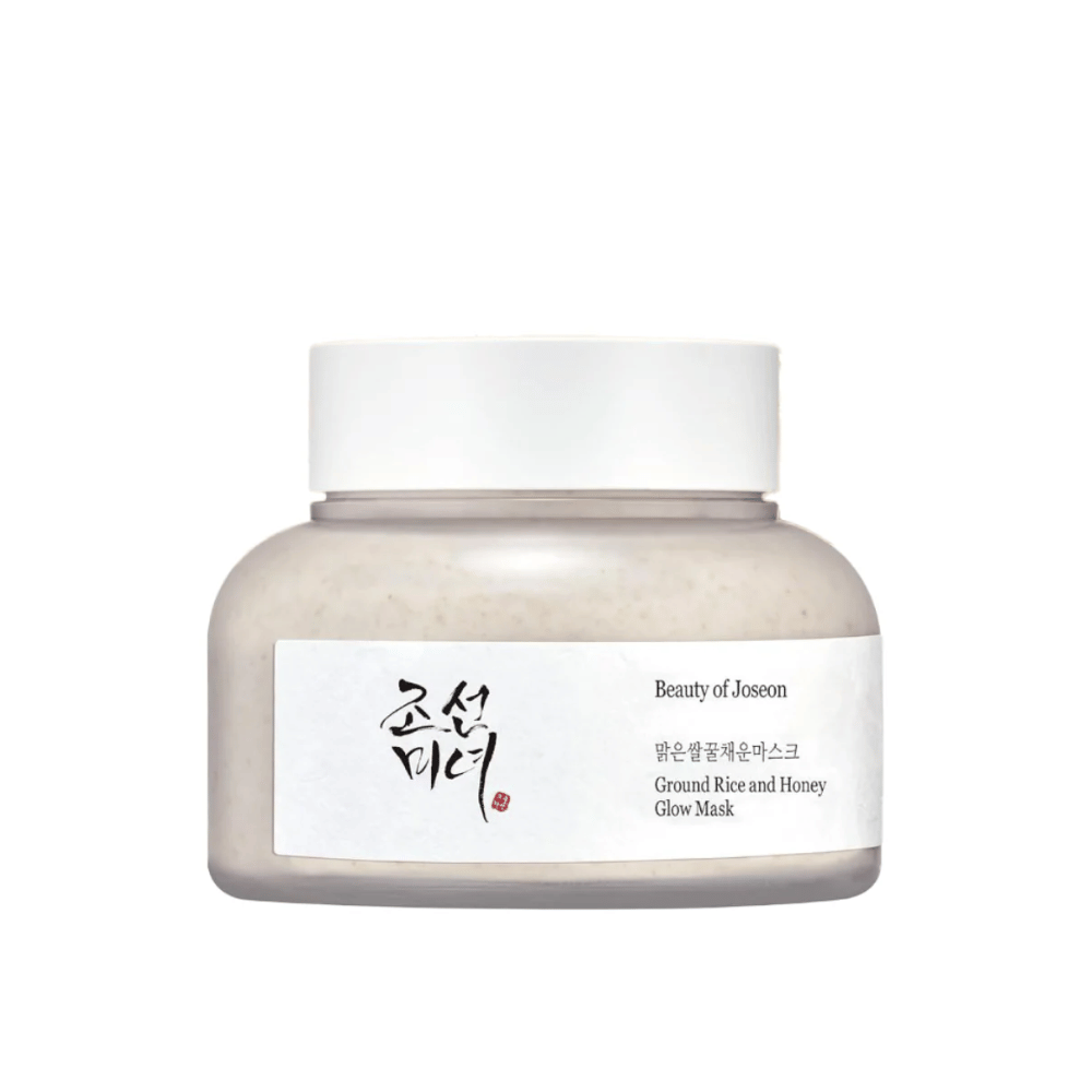 Um frasco "Beauty of Joseon Ground Rice and Honey Glow Mask". A embalagem é simples, com uma tampa branca e um rótulo que apresenta o nome do produto e os ingredientes em coreano e inglês. O produto é projetado para dar brilho e nutrição à pele.