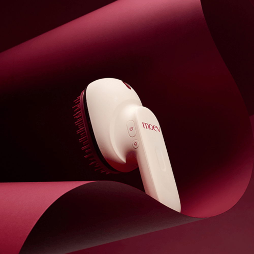 MOEV Hair Steamer Pro em design elegante contra fundo vermelho. Escova de cuidados capilares inovadora que usa vapor e calor para proporcionar brilho, suavidade e saúde capilar fortalecida.