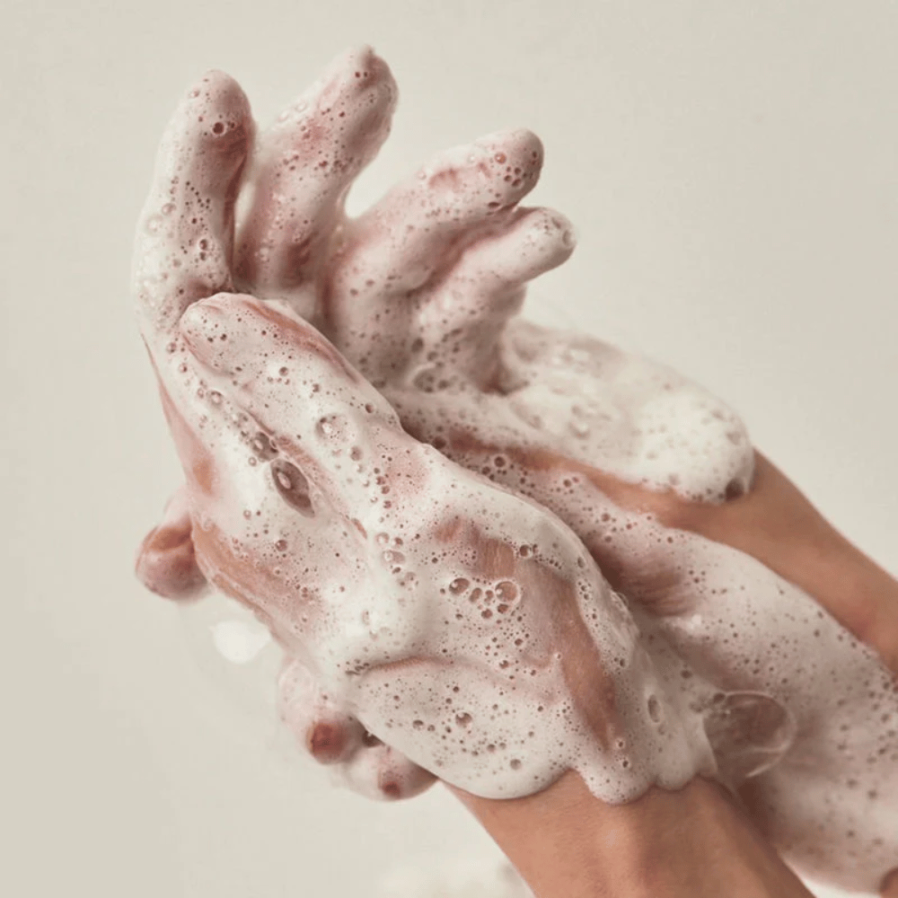 Imagem aproximada de mãos cobertas por uma espuma de limpeza rica e cremosa. A imagem ilustra a espuma e as propriedades de limpeza do produto, além de transmitir claramente uma sensação de utilização e textura.
