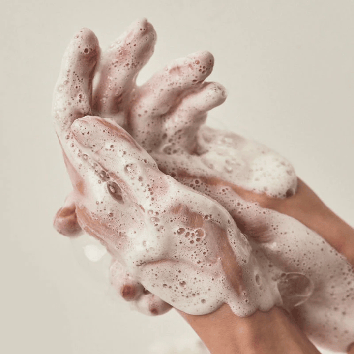 Imagem aproximada de mãos cobertas por uma espuma de limpeza rica e cremosa. A imagem ilustra a espuma e as propriedades de limpeza do produto, além de transmitir claramente uma sensação de utilização e textura.