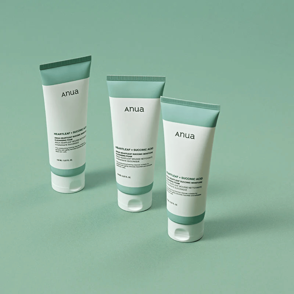 Três embalagens de Anua Heartleaf + Succinic Acid Moisture Cleansing Foam apresentadas sobre um fundo verde-claro. A imagem destaca o design limpo e minimalista do produto, além de transmitir uma impressão profissional da gama de produtos.