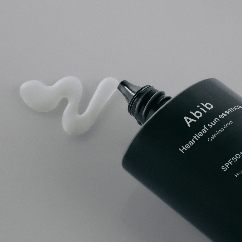 Close-up de Abib Heartleaf Sun Essence Calming Drop com o creme solar espremido em uma linha branca e ondulada sobre uma superfície clara.