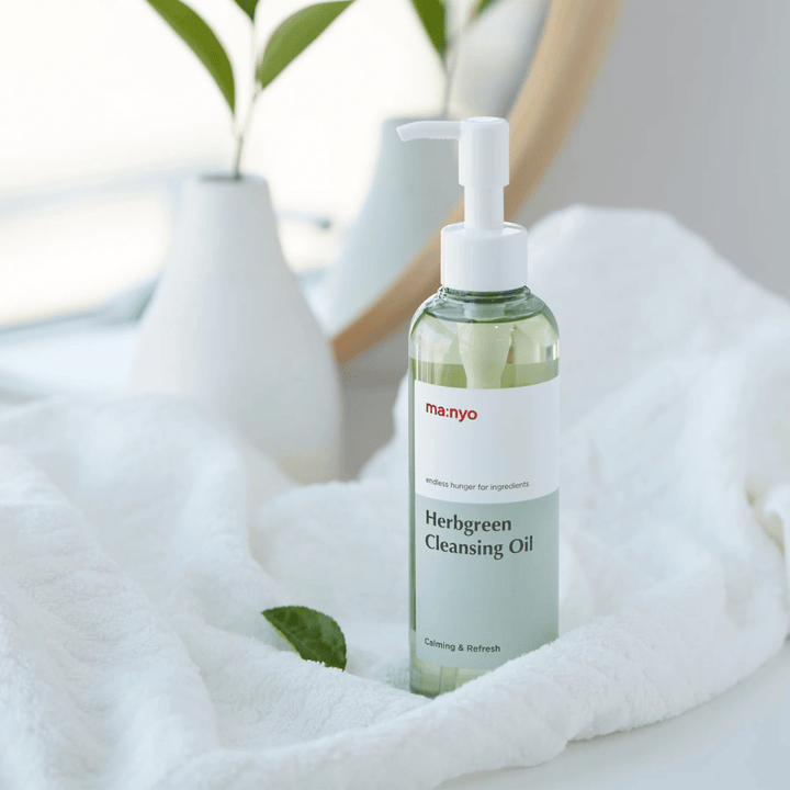ma:nyo Herbgreen Cleansing Oil em frasco com bomba colocado sobre toalha branca, óleo de limpeza calmante com ingredientes à base de ervas para uma limpeza facial suave