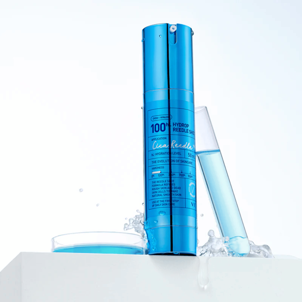 Garrafa azul VT Cica Hyalon Hydrop Reedle Shot 100hL em pé sobre superfície branca com respingos de água, ao lado de um tubo de ensaio cheio de líquido azul e uma tampa redonda com o mesmo líquido.