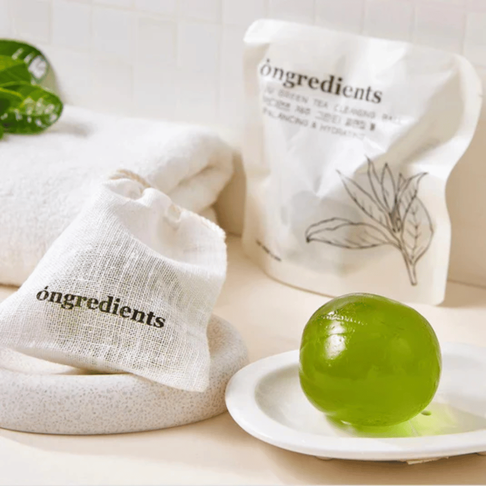 Óngredients Jeju Green Tea Cleansing Ball colocado em um prato com embalagem e toalha – limpeza suave com chá verde de Jeju.