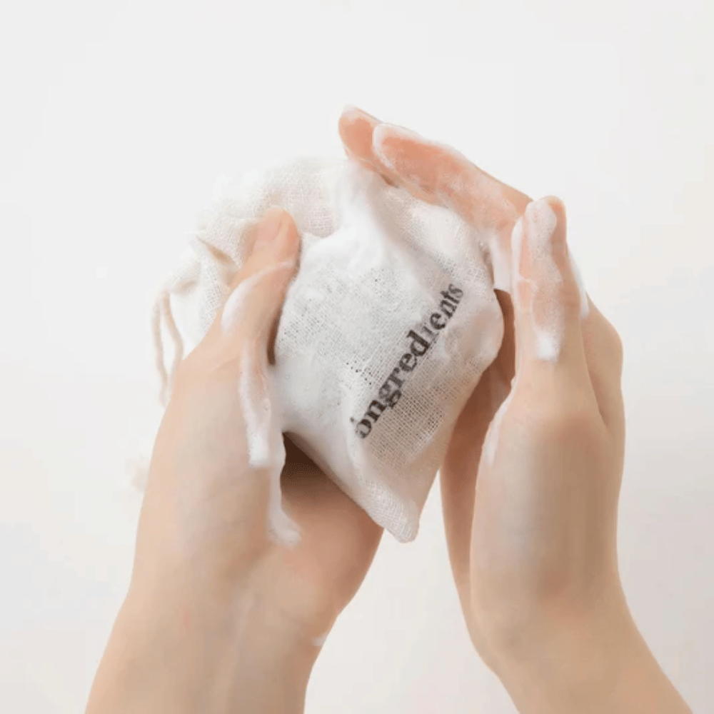Mãos ensaboando Óngredients Jeju Green Tea Cleansing Ball em bolsa de tecido – limpeza facial vegana com chá verde.
