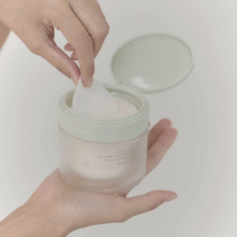 Mão pega uma almofada de toner do frasco Celimax Ji Woo Gae Cica BHA Blemish Toner Pad, perfeito para pele impura.