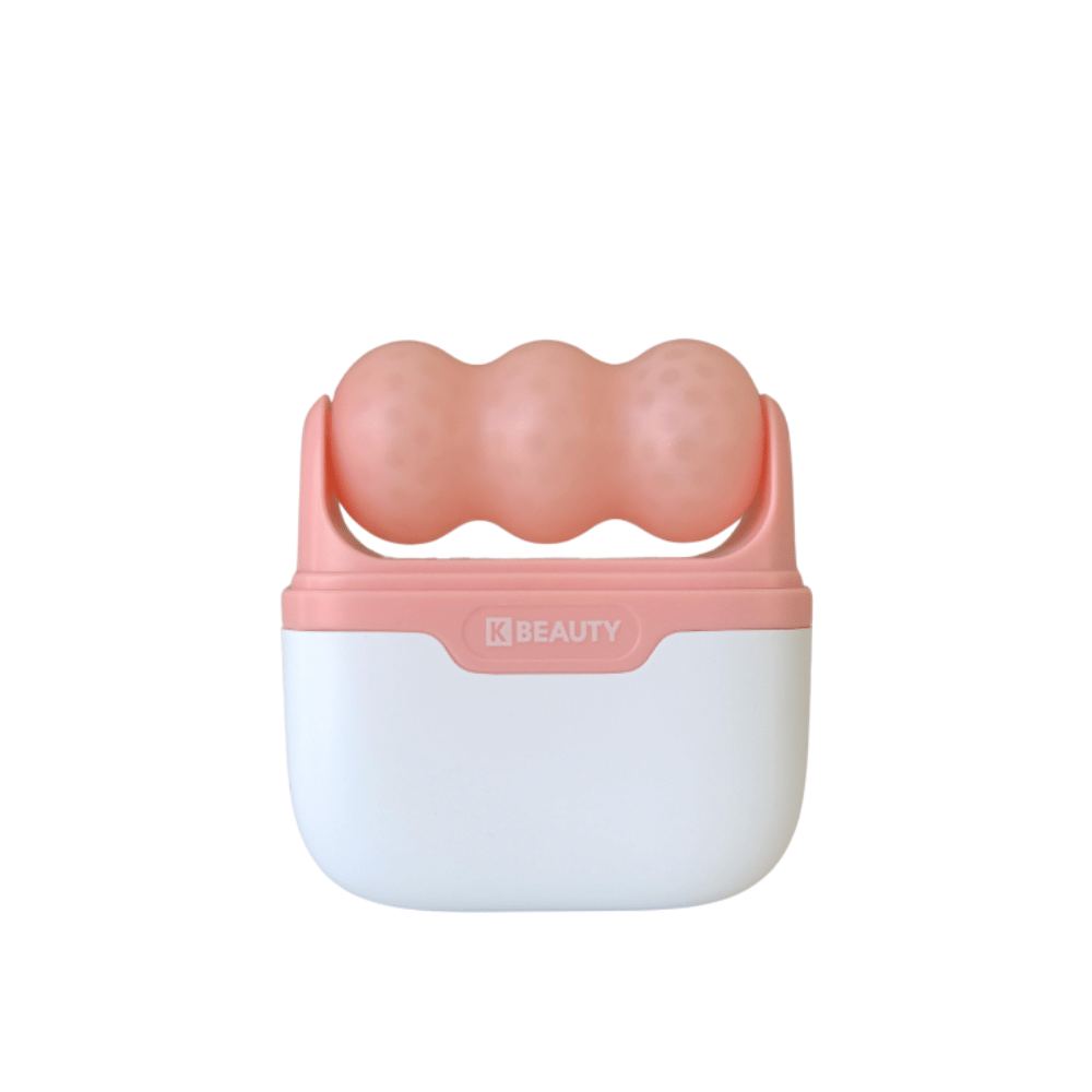 A imagem mostra um K-Beauty Ice Roller com uma alça branca e rosa. O produto tem três rolos arredondados e pontilhados em cor de rosa no topo, projetado para esfriar e massagear o rosto. O fundo é completamente branco.