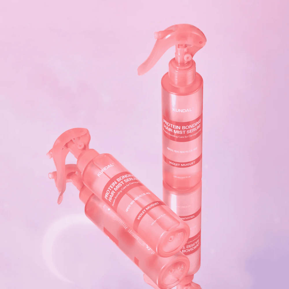 KUNDAL Protein Bonding Hair Mist Serum Violet Muguet em frascos spray rosa, em pé e deitado contra um fundo rosa claro com reflexo.