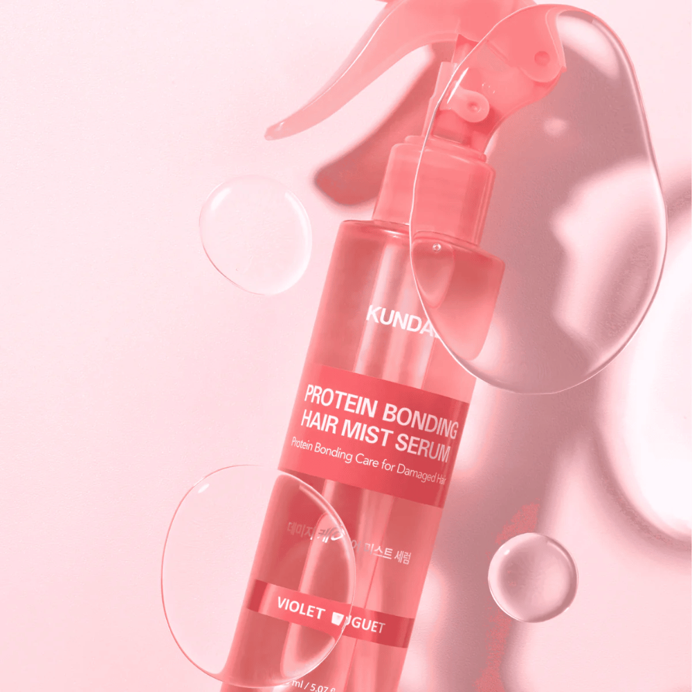 KUNDAL Protein Bonding Hair Mist Serum Violet Bouquet em frasco spray rosa, fotografado contra fundo rosa com gotas de água.