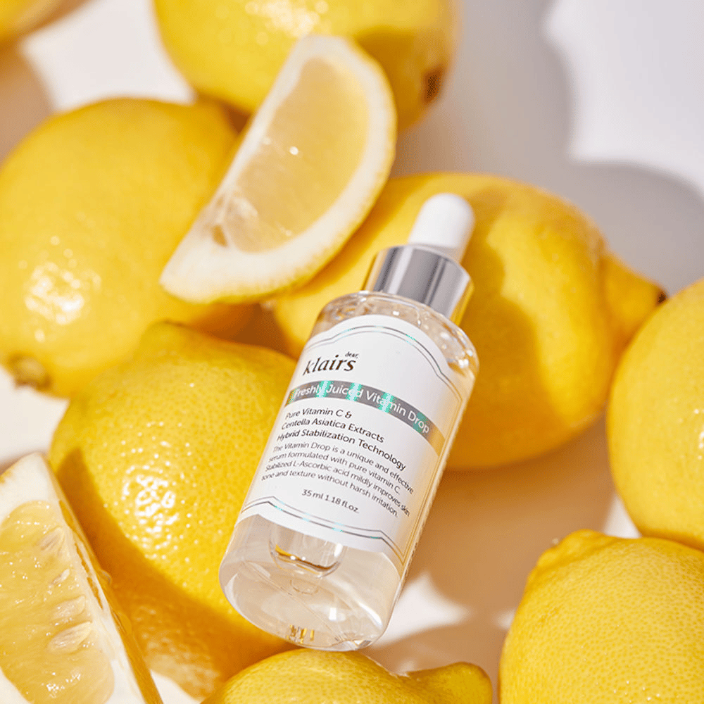 Klairs Freshly Juiced Vitamin Drop frasco de sérum rodeado por metades de limão fresco e fatias de limão sobre uma superfície clara, destacando os ingredientes.