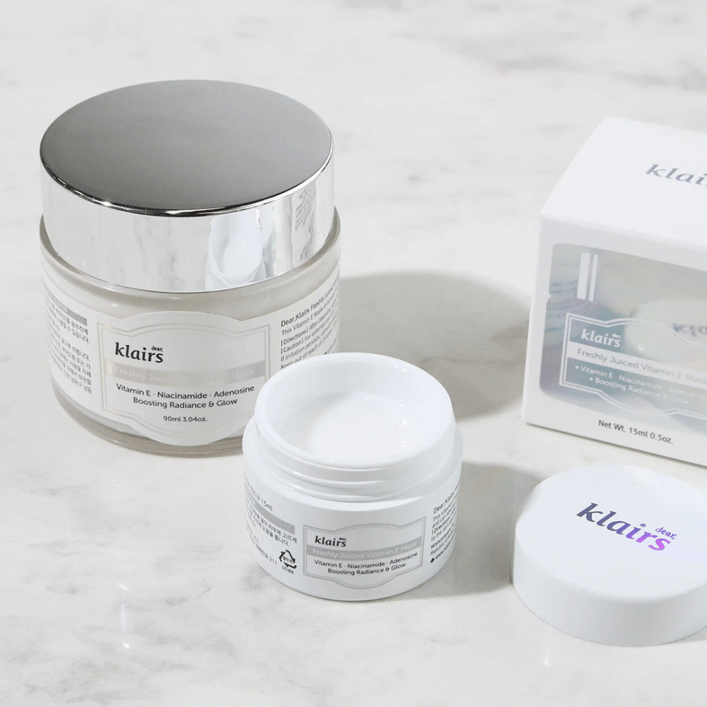 Uma coleção de produtos de cuidados com a pele da Klairs em um balcão de mármore: um frasco fechado, um frasco aberto com creme e uma caixa com texto.