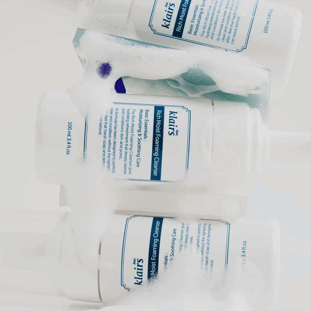 Três frascos de Klairs Rich Moist Foaming Cleanser cobertos com espuma e gotas de água, colocados sobre uma superfície branca.