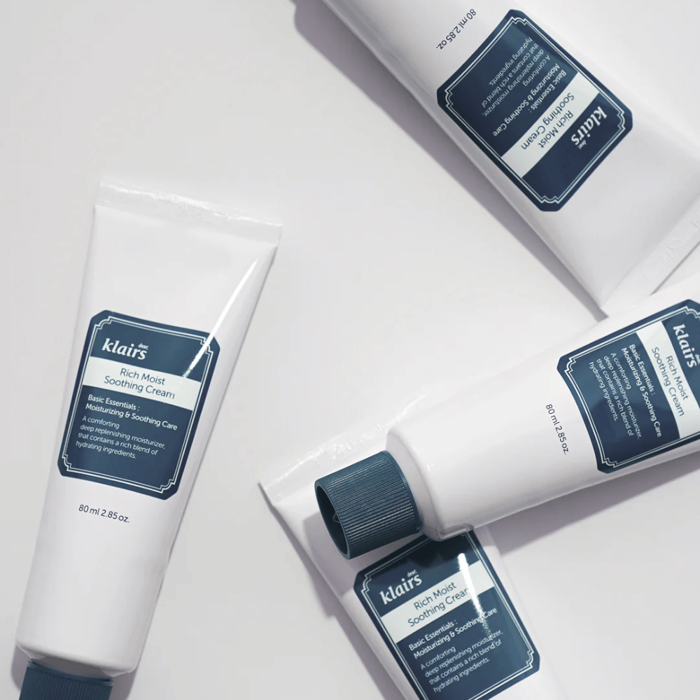 Vários tubos de Klairs Rich Moist Soothing Cream estrategicamente colocados em uma superfície clara, com sombras criando profundidade.