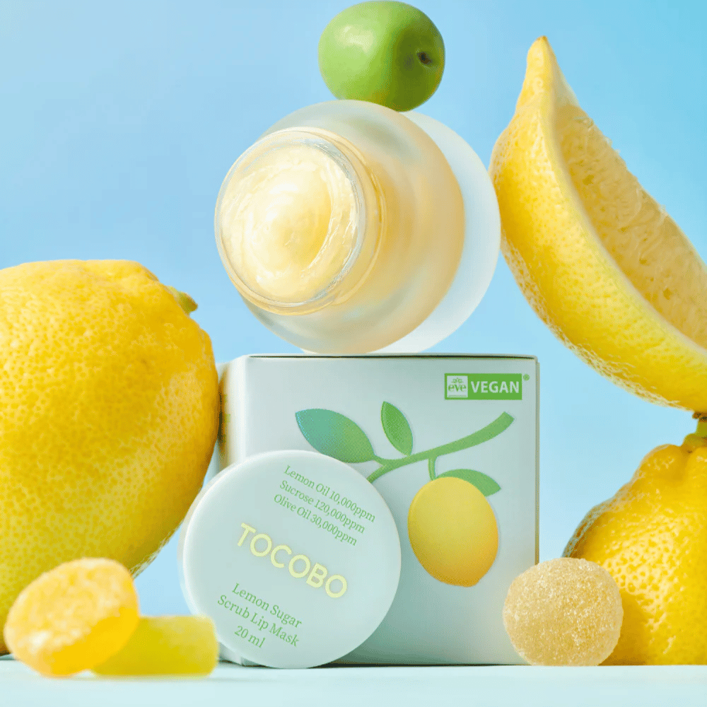 Frasco com Tocobo Lemon Sugar Scrub Lip Mask colocado entre limões e embalagem, marcado como amigo dos veganos.