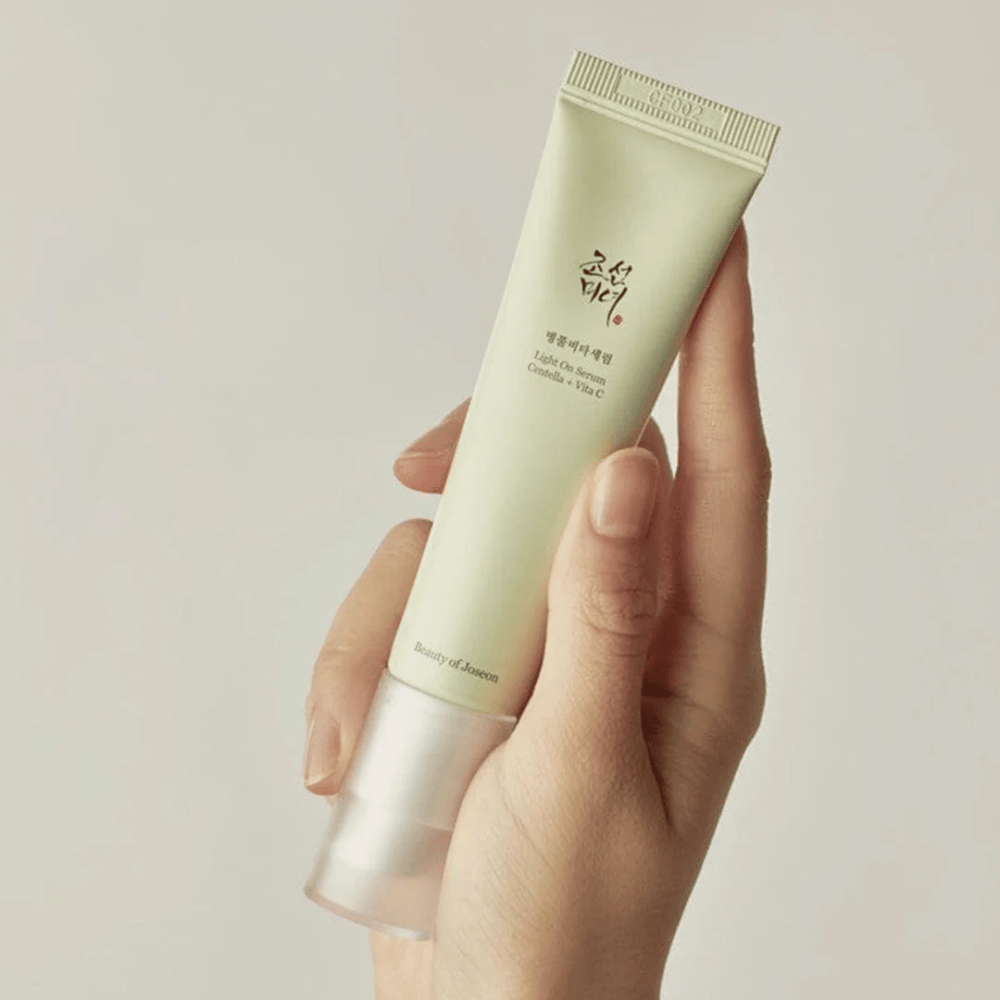 Uma mão segura o Beauty of Joseon Light On Serum com Centella e vitamina C, em um tubo verde-claro com design minimalista contra um fundo neutro.