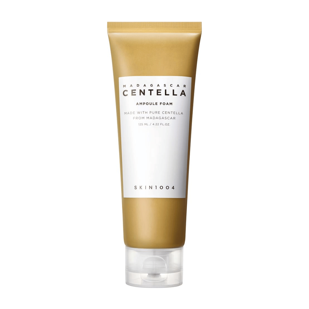 A imagem mostra um tubo de "Madagascar Centella Ampoule Foam" da marca SKIN1004. É um produto de limpeza facial que contém 125 ml / 4.22 fl.oz. A fórmula é baseada em Centella pura extraída de plantas em Madagascar. O produto é projetado para limpar e cuidar suavemente da pele.
