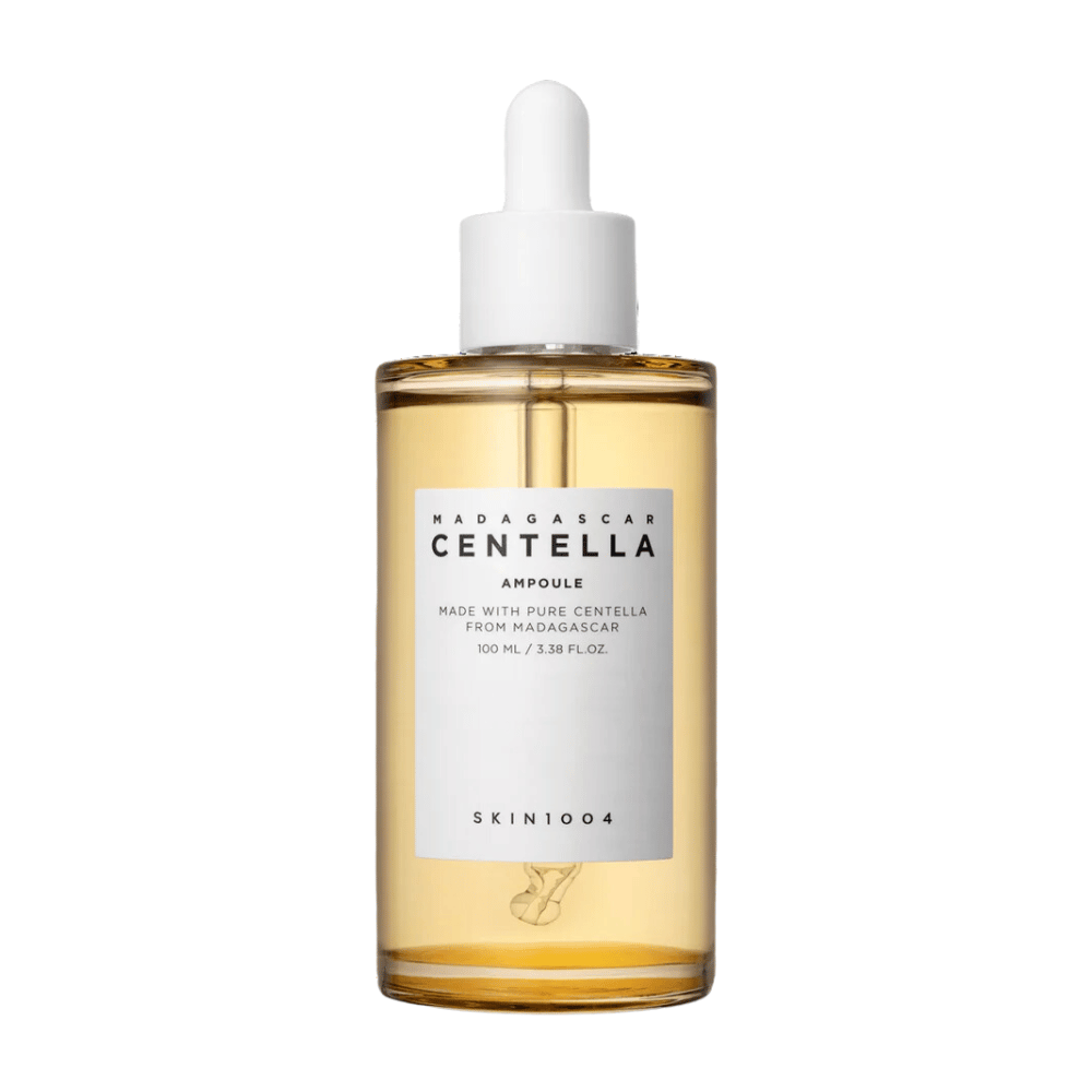 A imagem mostra uma garrafa de "Madagascar Centella Asiatica 100 Ampoule" de SKIN1004. A garrafa contém 100 ml e afirma ser feita com Centella pura de Madagascar. O produto parece ser um soro de cuidados com a pele e o rótulo simples dá uma impressão de pureza e naturalidade. A garrafa com conta-gotas sugere que este é um produto de cuidados com a pele cuidadosamente dosado.