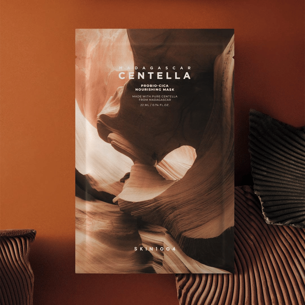 Embalagem de Sheet mask de SKIN1004 sobre um fundo castanho quente com design inspirado na natureza.