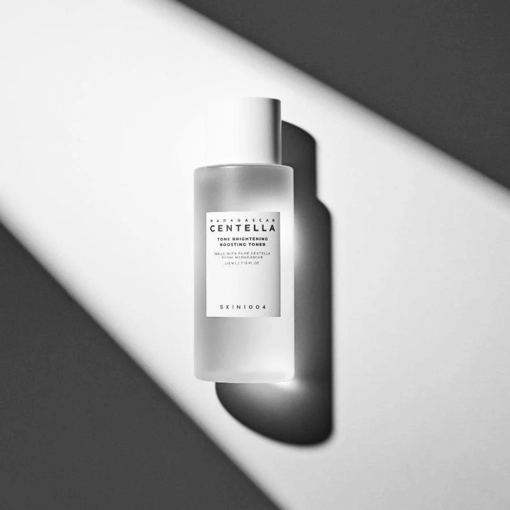 Frasco de SKIN1004 Madagascar Centella Tone Brightening Boosting Toner  deitado sobre uma superfície branca com sombra dramática em jogo de luz preto e branco.