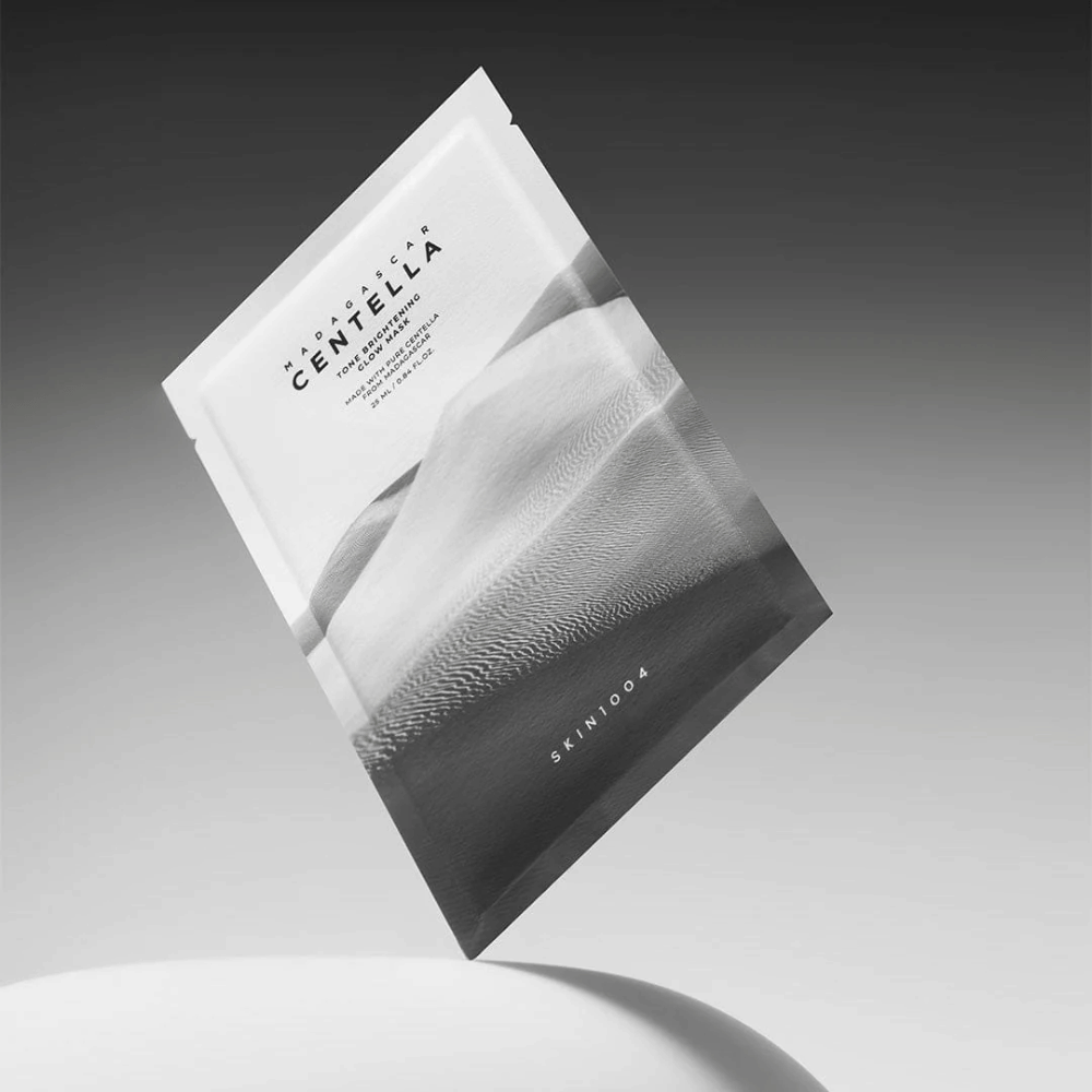 Embalagem de Sheet mask de SKIN1004 a flutuar sobre um fundo cinzento com design minimalista.
