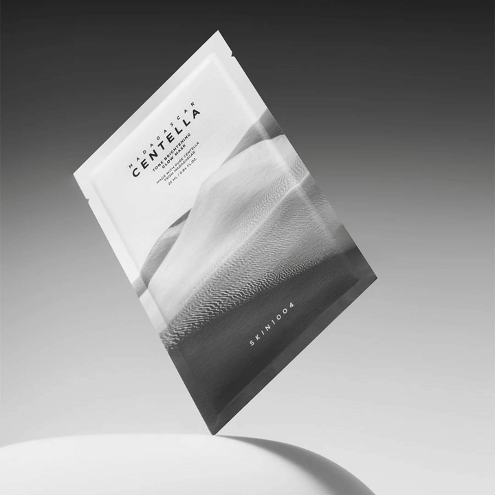 Embalagem de Sheet mask de SKIN1004 a flutuar sobre um fundo cinzento com design minimalista.