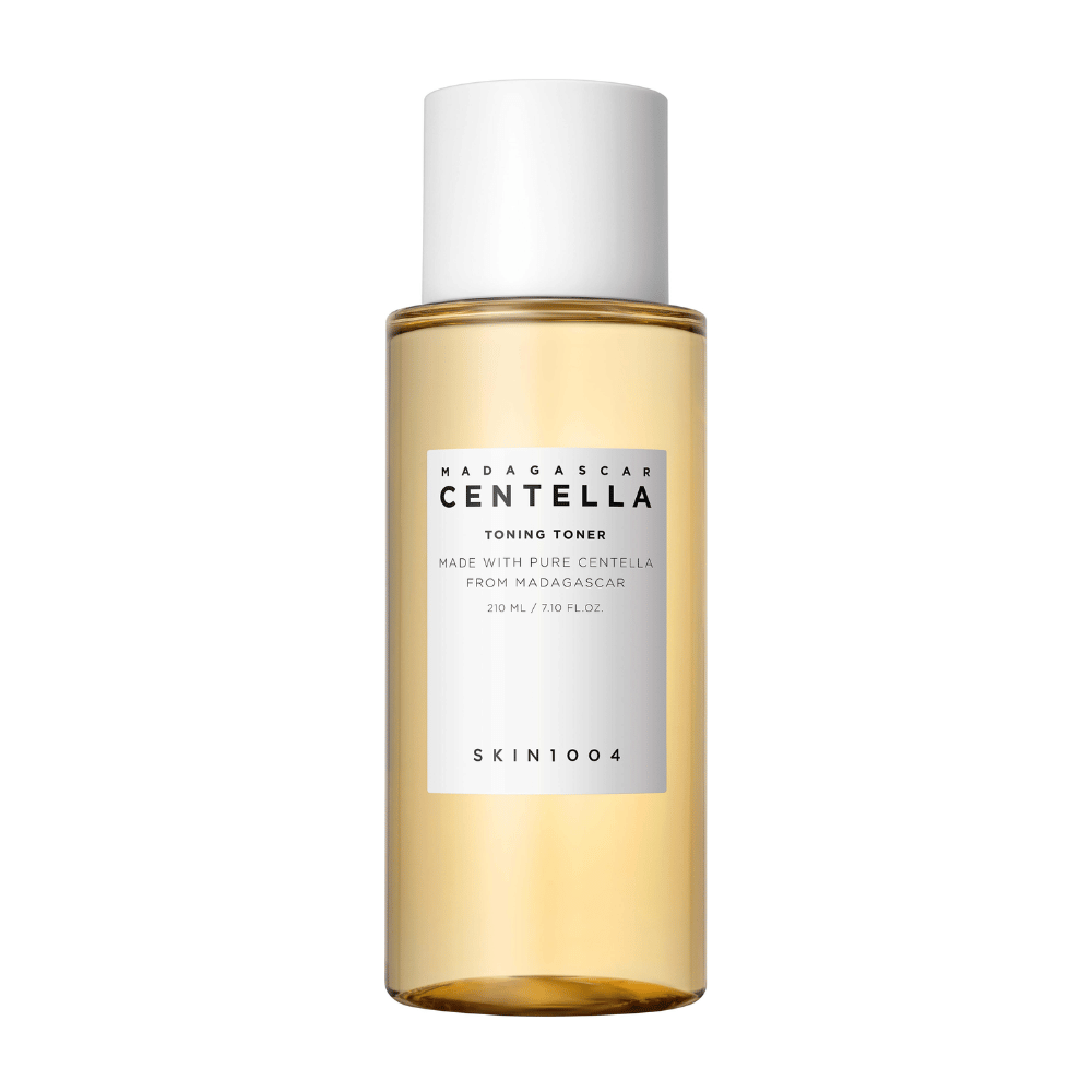 A imagem mostra uma garrafa com tons de cuidados para a pele, marcada "Madagascar Centella Toning Toner" de SKIN1004. O produto é indicado como contendo 210 ml ou 7.10 fl.oz e é fabricado com Centella pura de Madagascar. A embalagem é simples e elegante com uma garrafa transparente e líquido dourado dentro, o que dá uma sensação de luxo e pureza. O logotipo da marca SKIN1004 é claramente visível na parte inferior do rótulo.