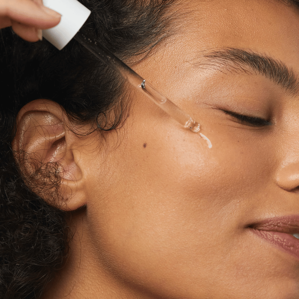 Mulher aplicando Skin1004 Madagascar Centella Hyalu-Cica First Ampoule na bochecha com uma pipeta.