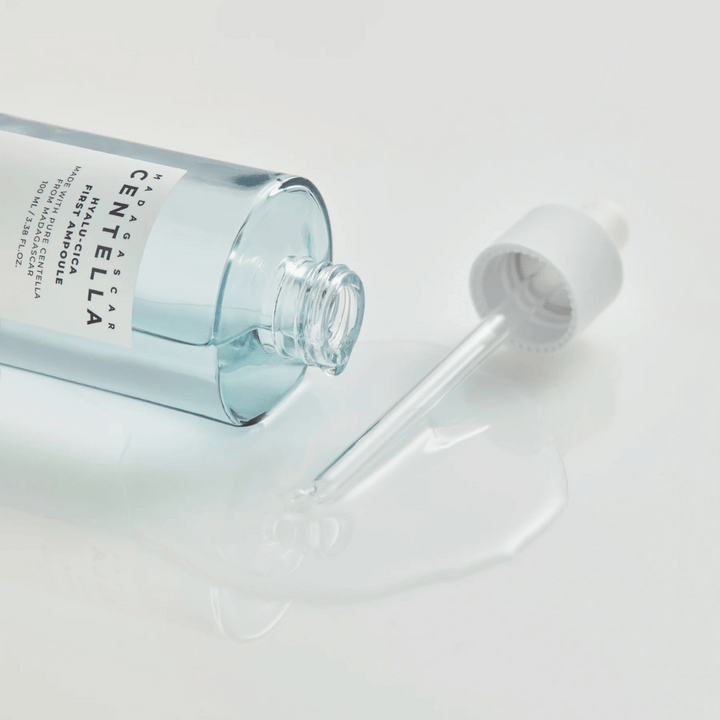 Närbild på öppen flaska Skin1004 Madagascar Centella Hyalu-Cica First Ampoule med pipett liggande och serum utspritt på vit yta.