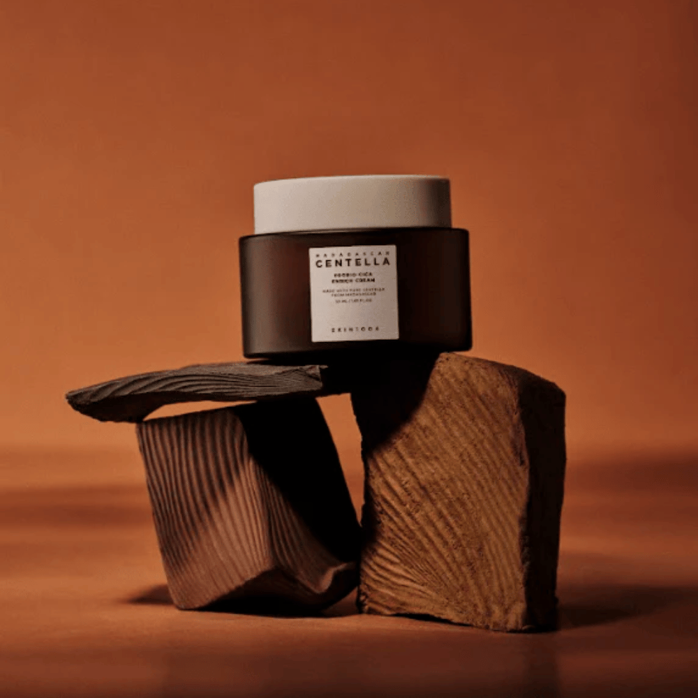 SKIN1004 Madagascar Centella Probio-Cica Enrich Cream em um elegante frasco de vidro marrom sobre blocos de madeira decorativos – creme facial coreano nutritivo que fortalece a barreira da pele.