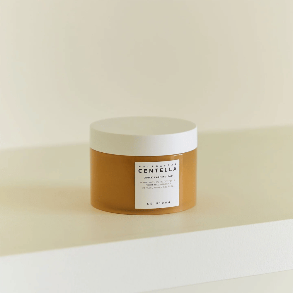 SKIN1004 Madagascar Centella Quick Calming Pad colocado em prateleira branca – pote de cor âmbar com tampa branca e etiqueta visível na frente.