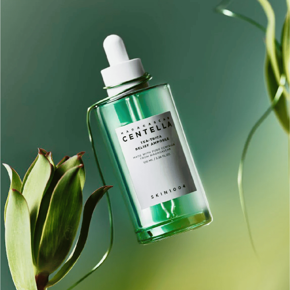SKIN1004 Madagascar Centella Tea-Trica Relief Ampoule – garrafa de vidro verde com pipeta, rótulo branco e conteúdo de 100 ml, fotografada contra um fundo verde com detalhes de plantas.